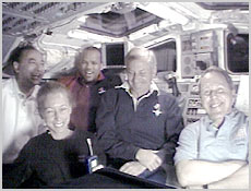 The STS-98 Astronauts (from left) Mark Polansky, Marsha Ivins, Robert Curbeam, Kenneth Cockrell and Thomas Jones talk to reporters on Earth from the shuttle's flight deck. NASA image.